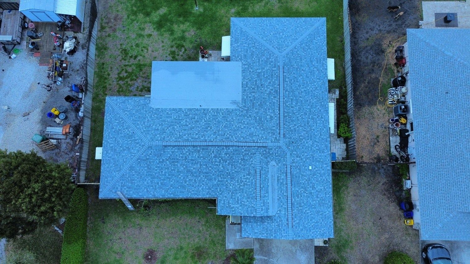 Aerial view of a blue-shingled house roof with surrounding yard and neighboring buildings.