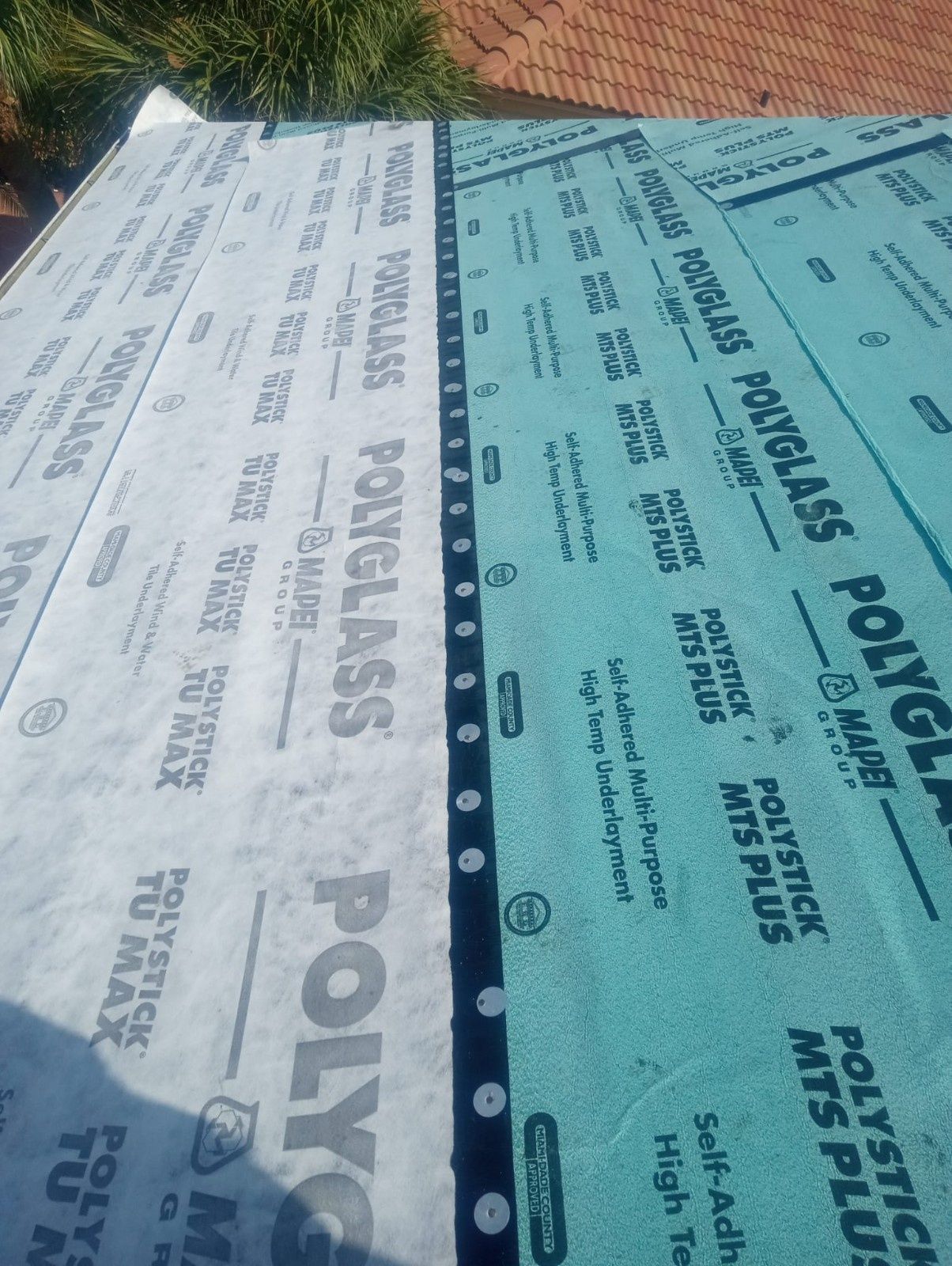 Stacks of white and green Polyglass roofing membrane sheets laid outdoors, with printed branding visible