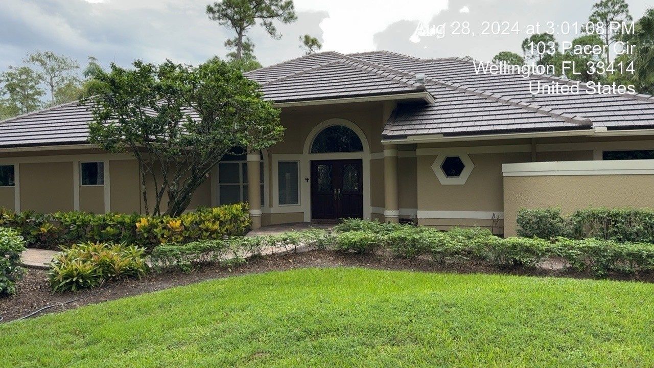 Single-story beige house with arched entry, dark roof, and manicured lawn under a cloudy sky