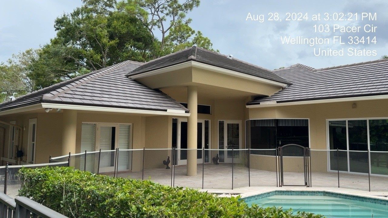 Single-story beige house with gray tiled roof, screened patio, and pool behind trimmed hedges