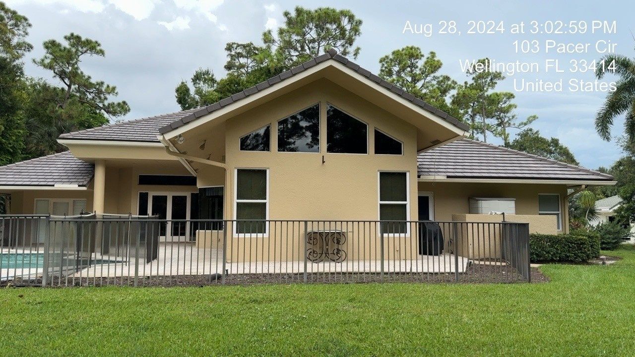 Single-story beige house with a large front porch, black railings, and a green lawn under a cloudy sky