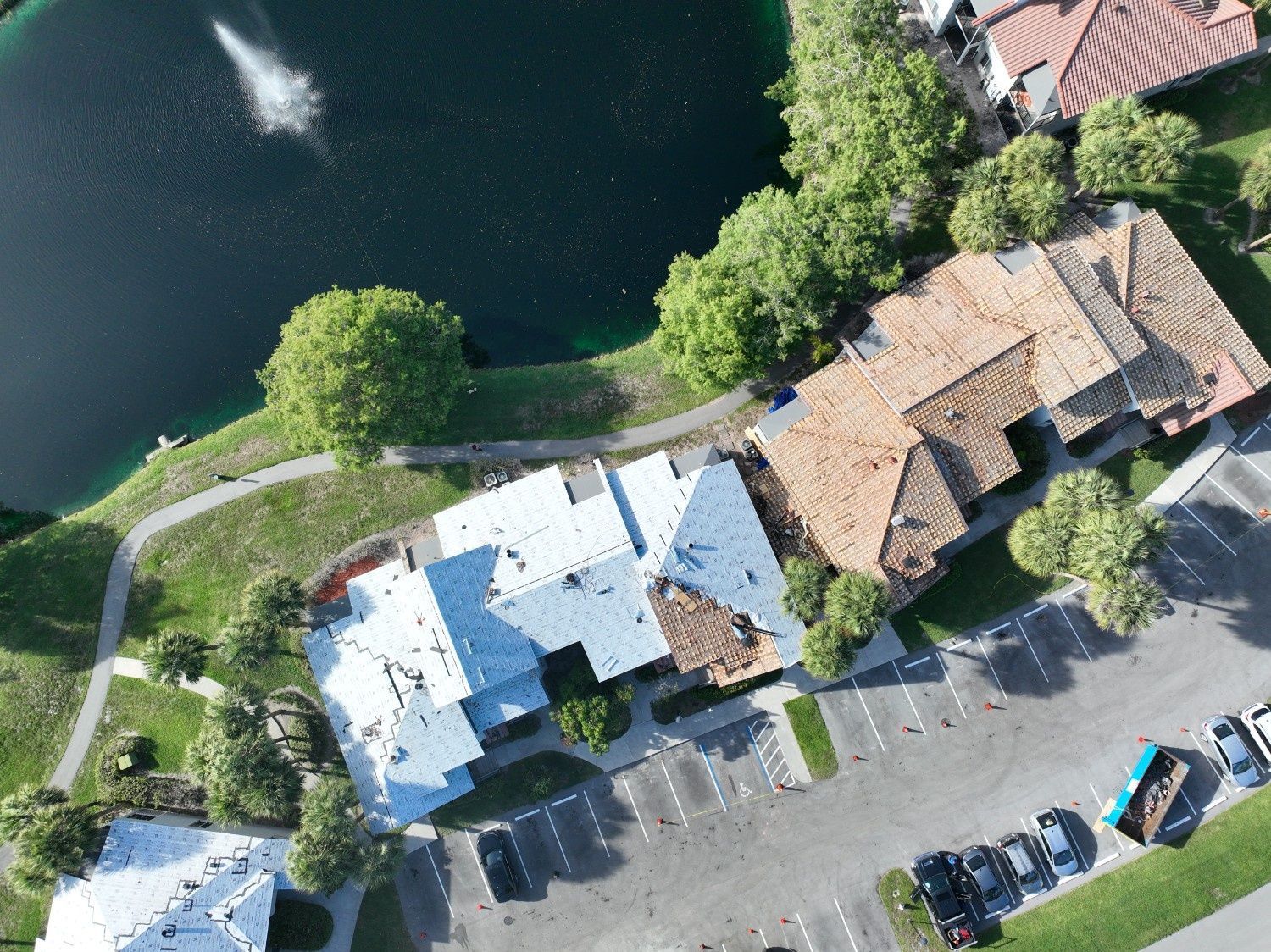Aerial view of a lakeside building with parked cars, trees, and a curved path along the water