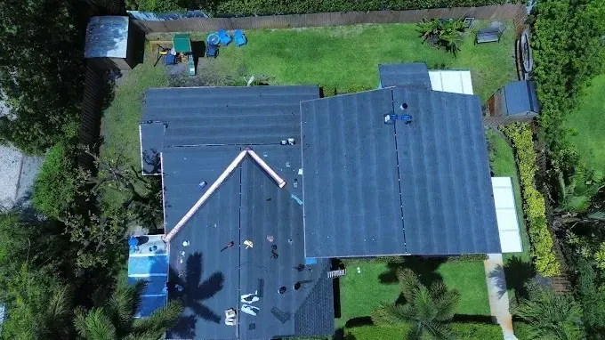 Aerial view of a house with a dark roof, green yard, and trees around it