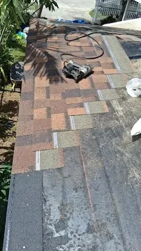 Roof under repair with asphalt shingles, a power tool, and coiled hose on a sloped rooftop