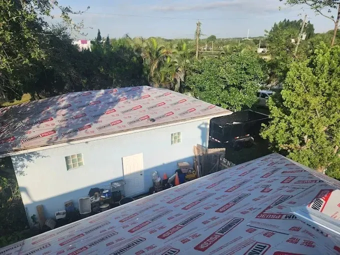 Two white houses with silver-red roofs amid lush green trees under a bright sky.