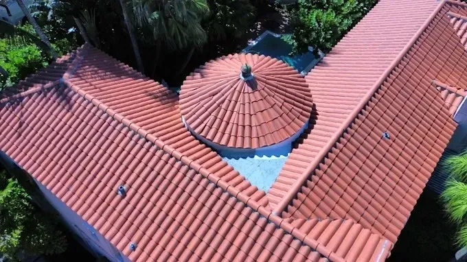 Aerial view of a red-tiled roof with a central round turret, surrounded by trees.