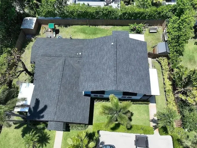 Aerial view of a house with a dark roof, surrounded by a green yard and trees.