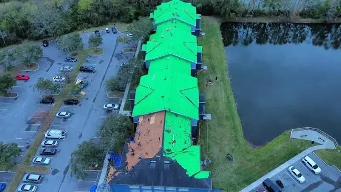 Aerial view of a long building with bright green roof beside a parking lot and a pond.