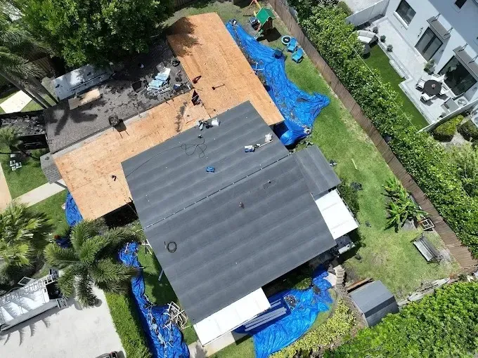 Aerial view of a house roof with blue tarps, surrounded by trees and neighboring homes