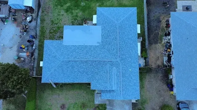 Aerial view of a blue-roofed house with surrounding trees and neighboring buildings