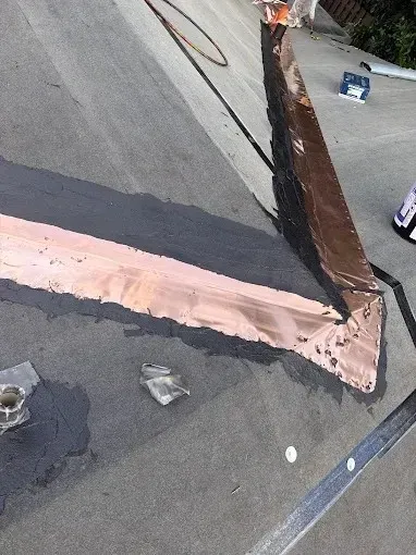 Close-up of a roof seam with pink flashing and dark sealant on gray roofing material