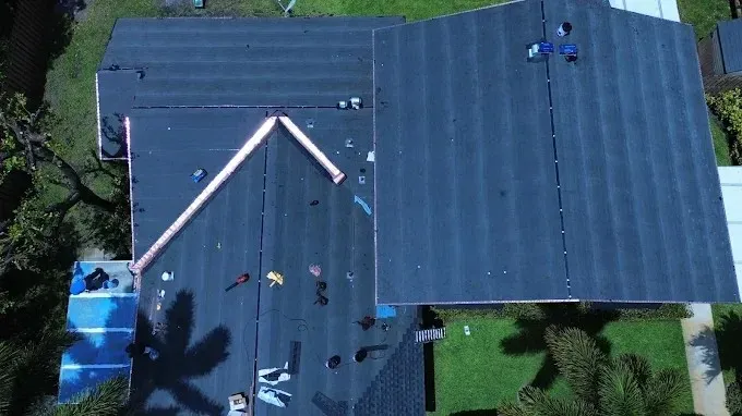 Aerial view of a dark roof with workers and light-colored roof beams near a tree-lined yard
