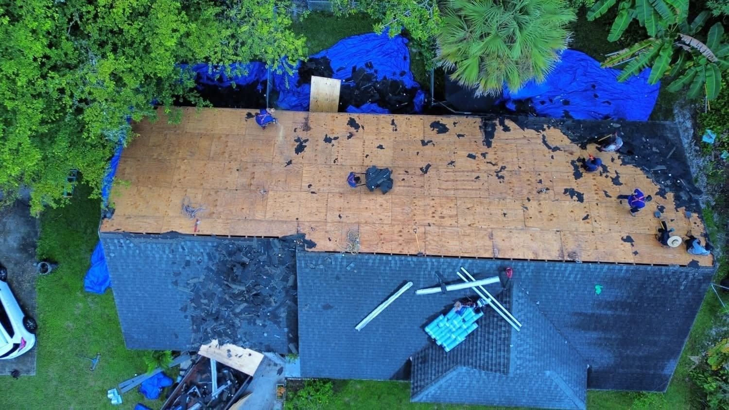 Aerial view of a damaged house roof with blue tarps and debris scattered on top.