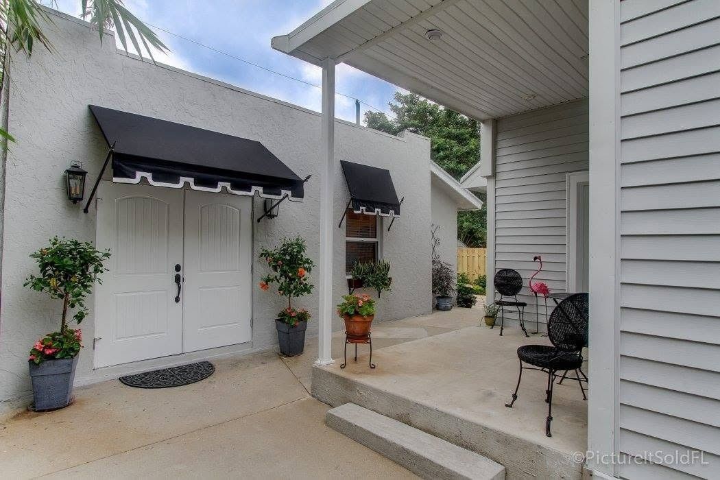 Covered patio with white doors, black awnings, potted plants, and a small table and chairs