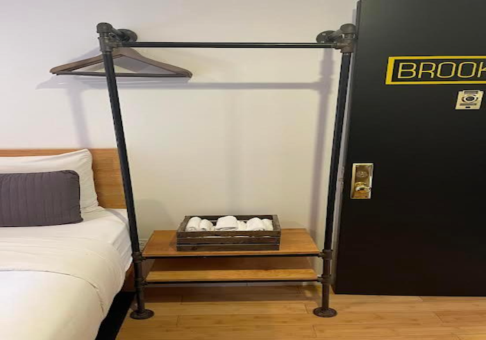 Black metal clothing rack beside a bed and dresser in a hotel room