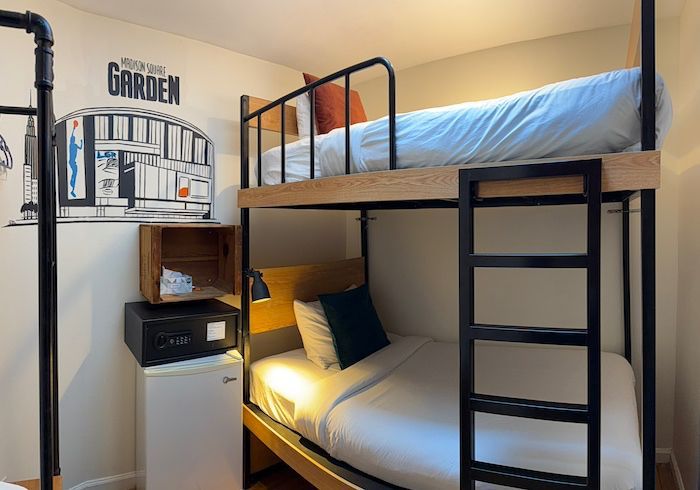 Small bedroom with a black metal bunk bed, white bedding, wooden desk nook, and a black-and-white wall poster