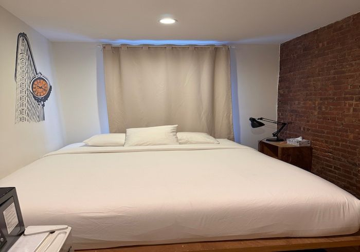 Minimal bedroom with a large white bed, beige curtains, and a brick accent wall