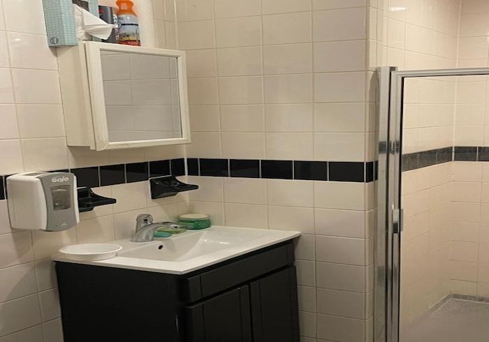 Bathroom sink and mirror with black cabinet, white tile walls, and a glass shower door