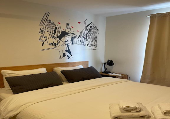 Neatly made bed in a minimalist bedroom with wall art, bedside lamp, and beige curtains