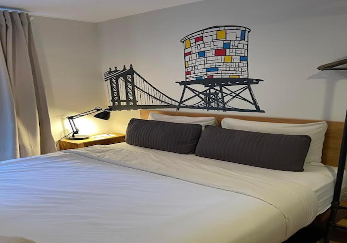 Bedroom with a neatly made bed, dark pillows, and a bridge mural above the headboard