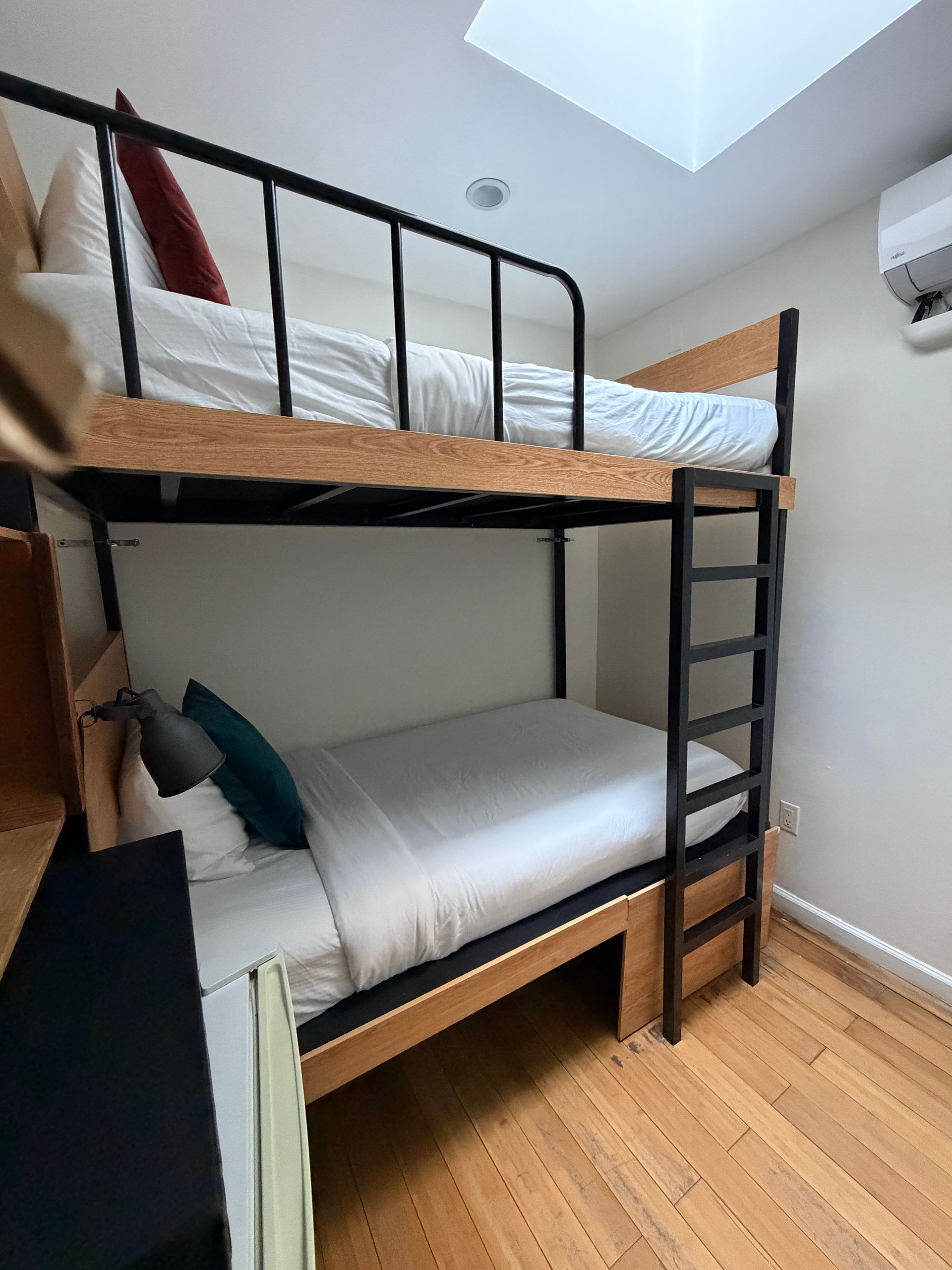 Small bedroom with black metal bunk beds, white bedding, and wood floor under a skylight.