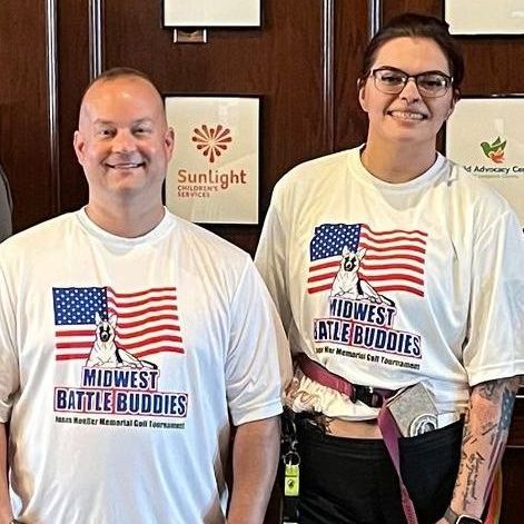 Two smiling people wear Midwest Battle Buddies t-shirts
