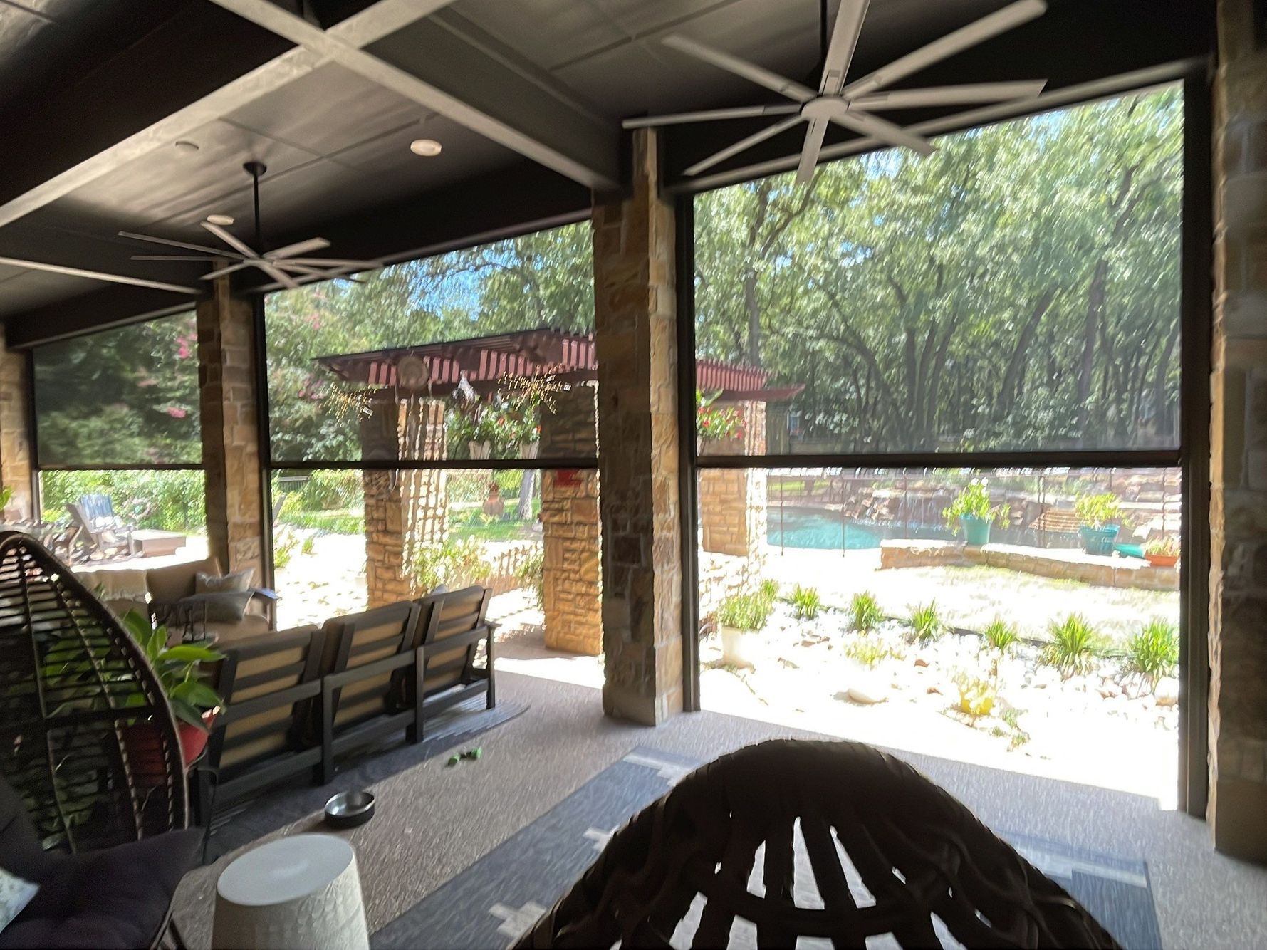 Outdoor patio with sun screens, a view of a yard, seating, ceiling fans, and stone pillars.