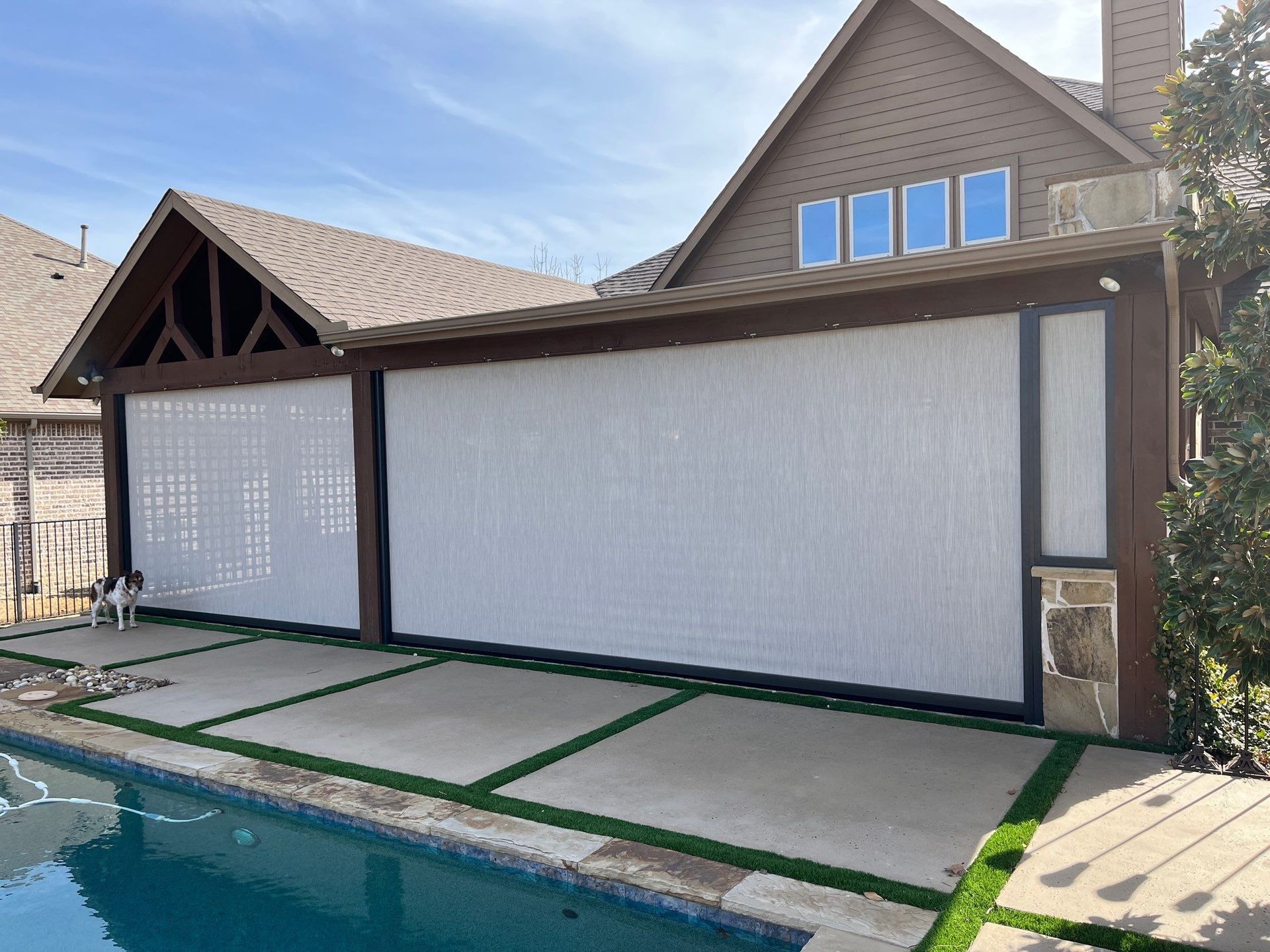 Backyard pool beside a covered patio with roll-down screens and stone paving