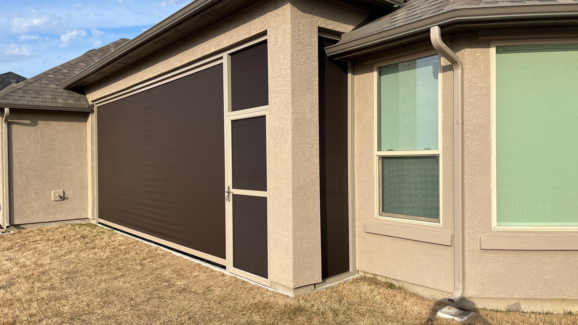 Brown outdoor screen on a beige house exterior. Beside a window with green tint.