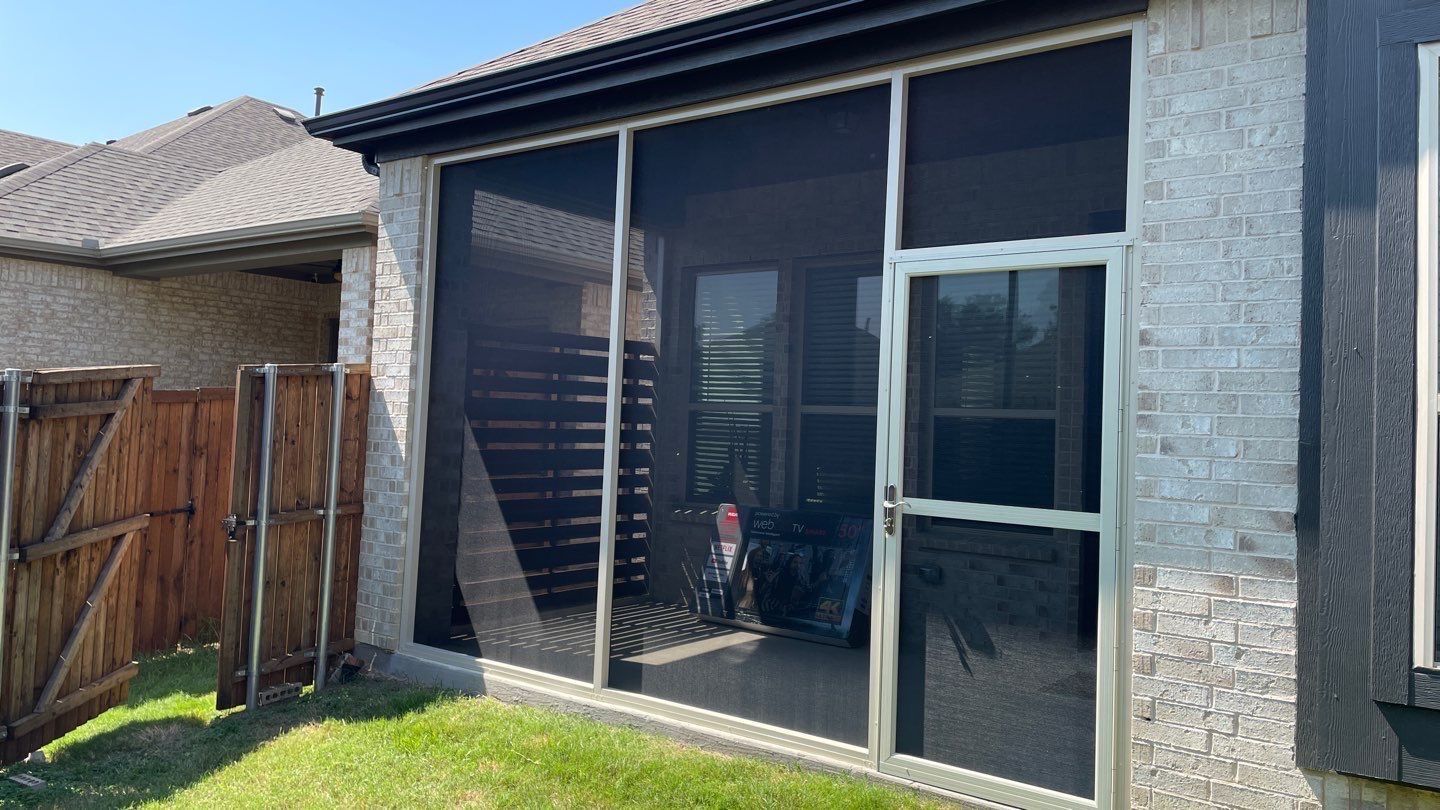 Screened patio with brick and wooden fence, dark screen doors and windows, green grass.