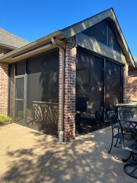 Screened-in patio with dark screens, brick columns, and a light-colored concrete patio floor. Blue sky visible.