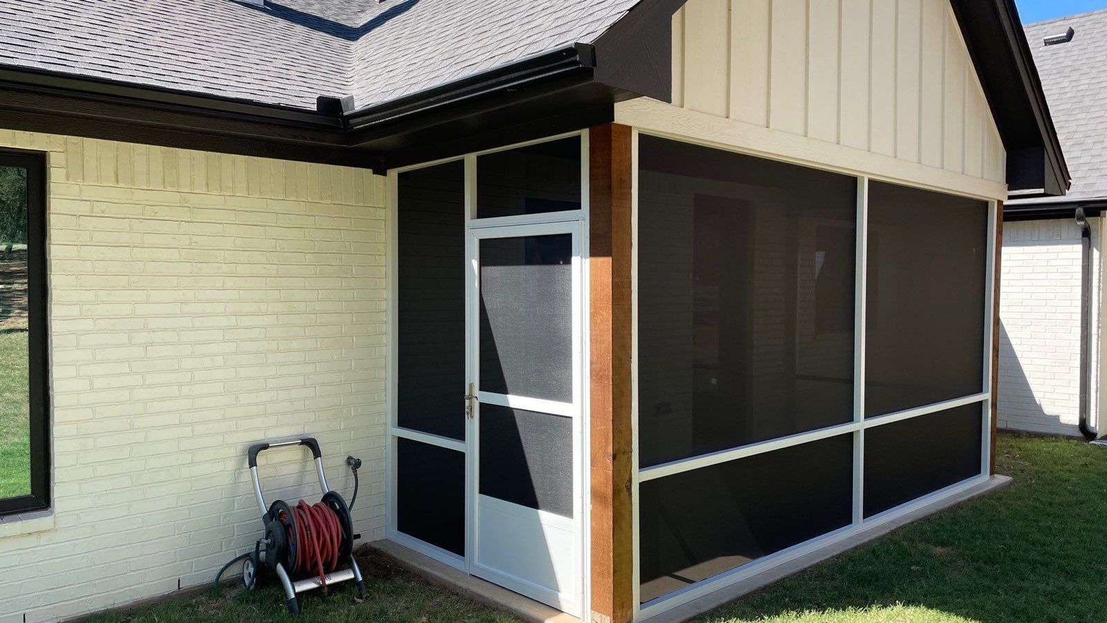Screened-in porch on a brick house; black screens, white trim, and a dark brown door frame.