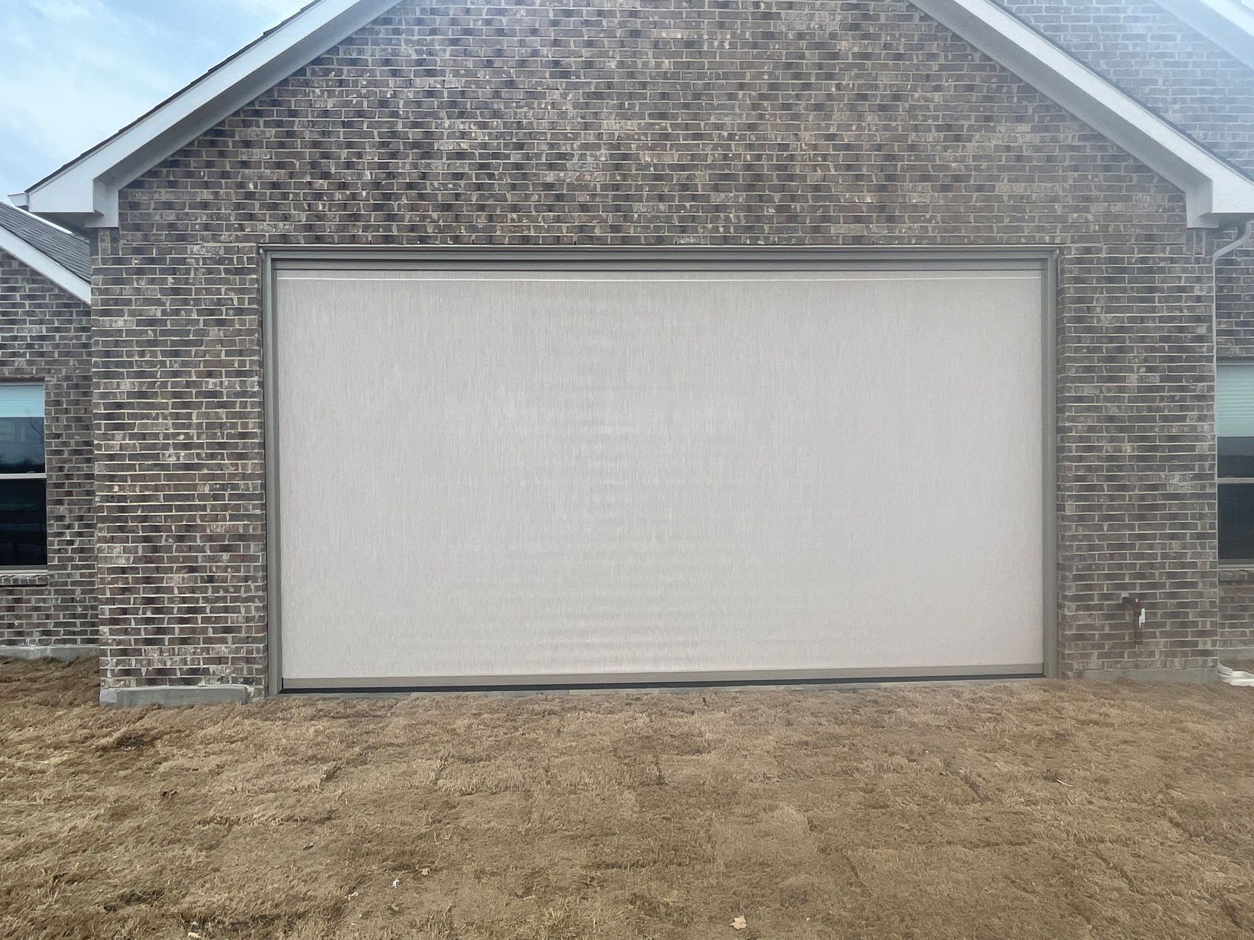 Garage door covered with a light-colored, textured screen against a brick wall.