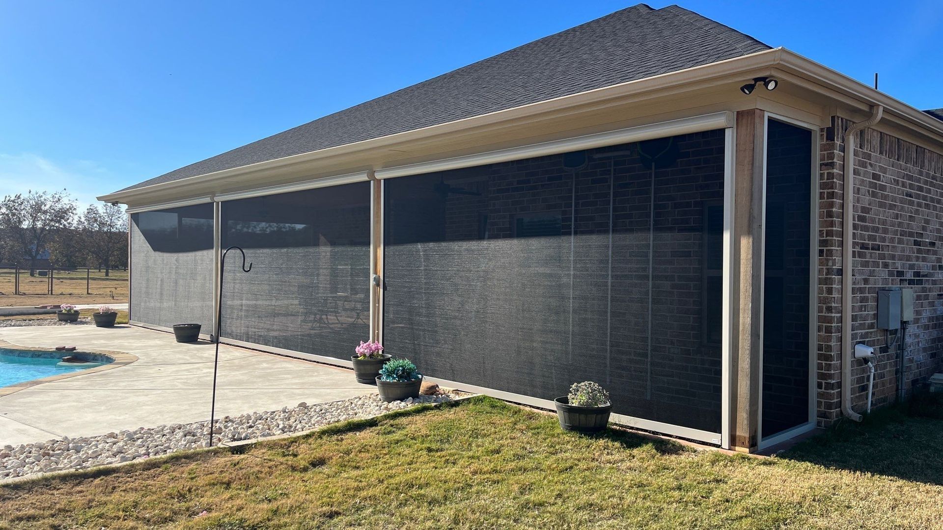 Screened patio area next to a pool. Black screens, beige trim, brick wall, and sunny day.