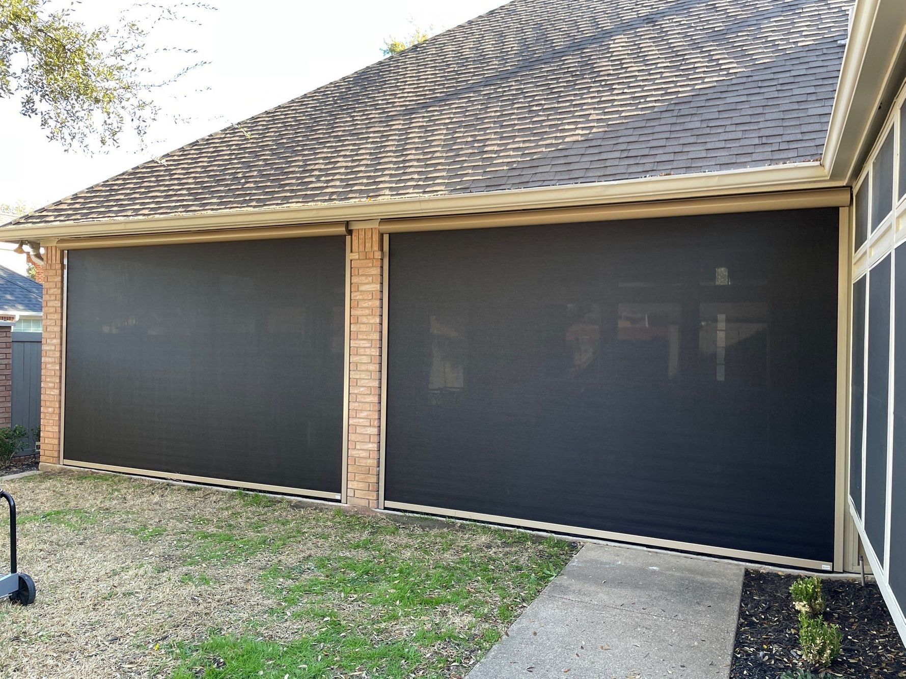 Outdoor patio with two large black screens installed between brick columns, under a shingled roof.