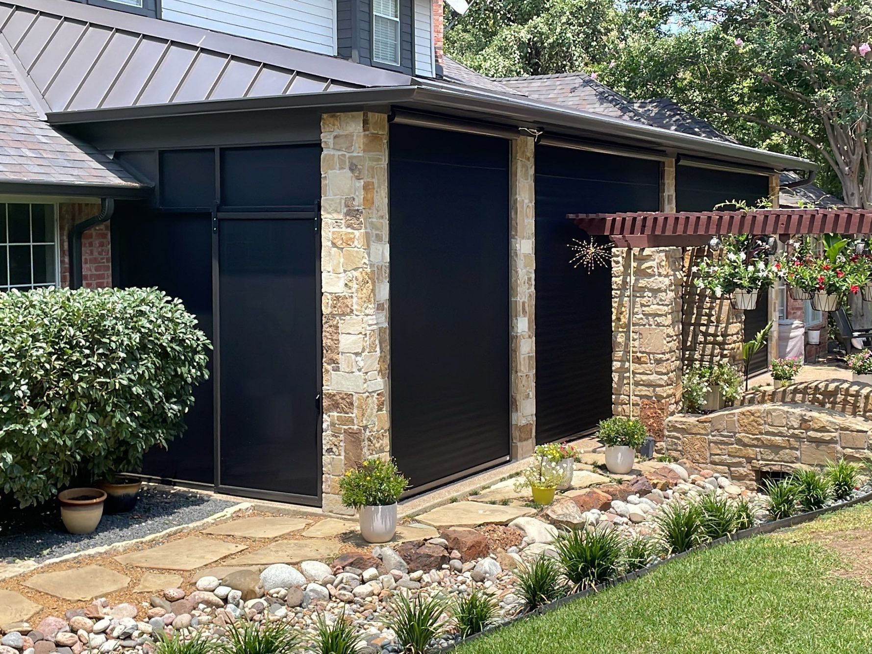 Black roll-down shutters on a house with stone accents, a walkway, and landscaping.