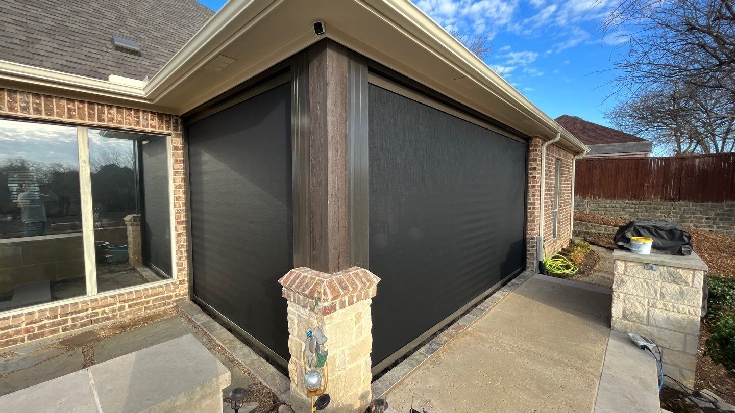 Exterior of a house with black roller shades installed on a patio, sunny day.