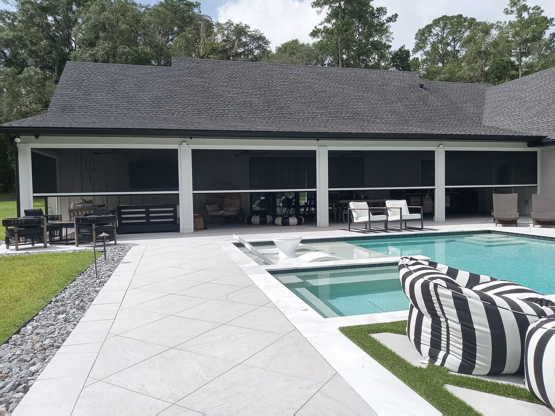 Poolside patio with retractable screens. Black screens, white columns, swimming pool, black and white striped seating.