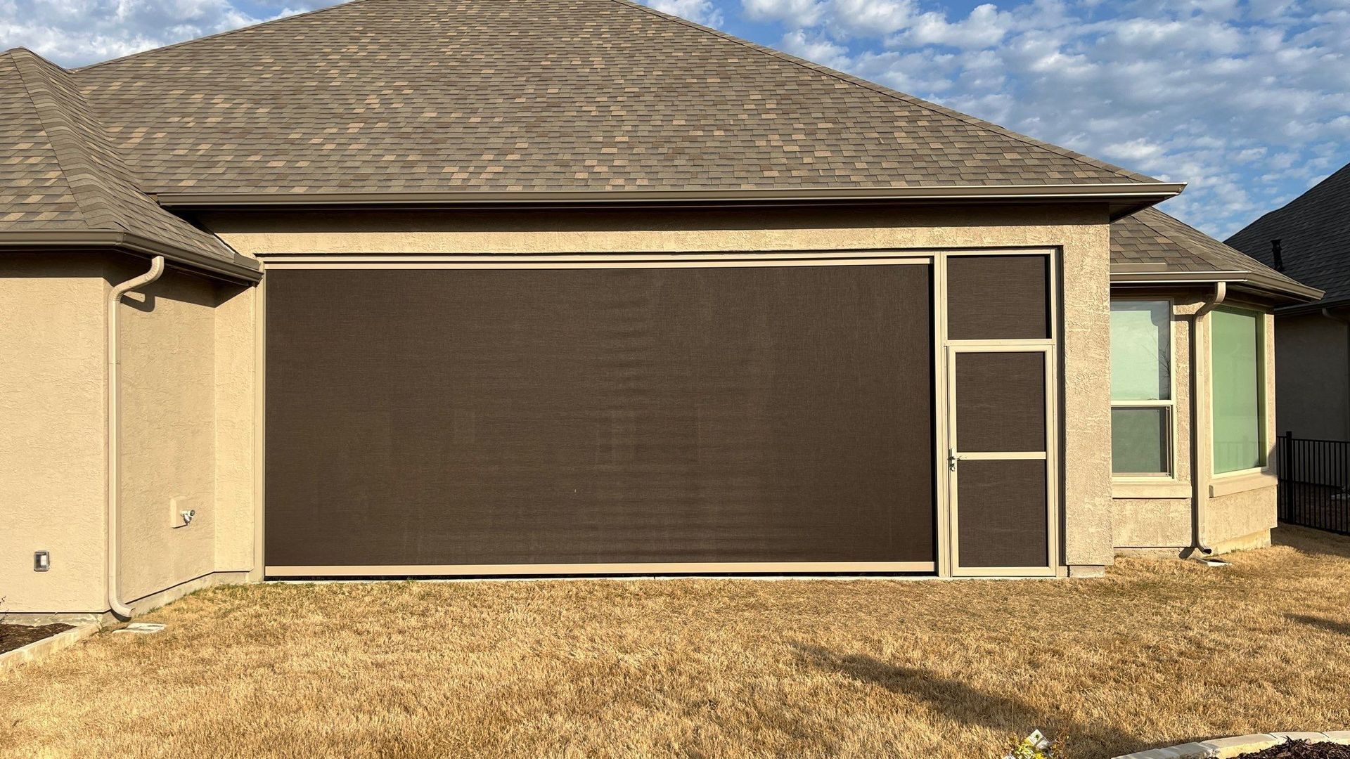 Brown retractable screen on a beige house, over a dry grass yard.