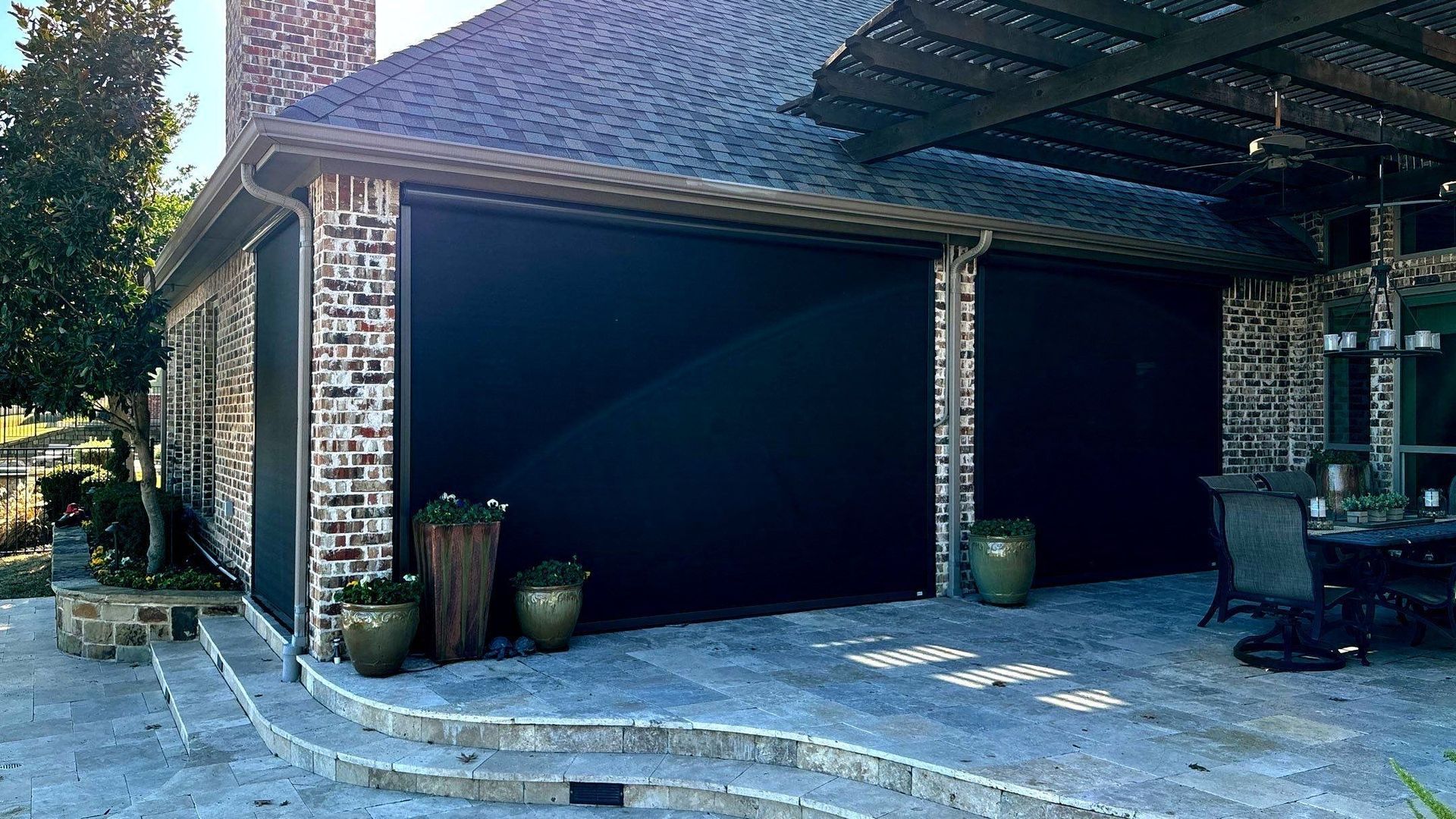 Black exterior sun shades on a brick house with a stone patio.
