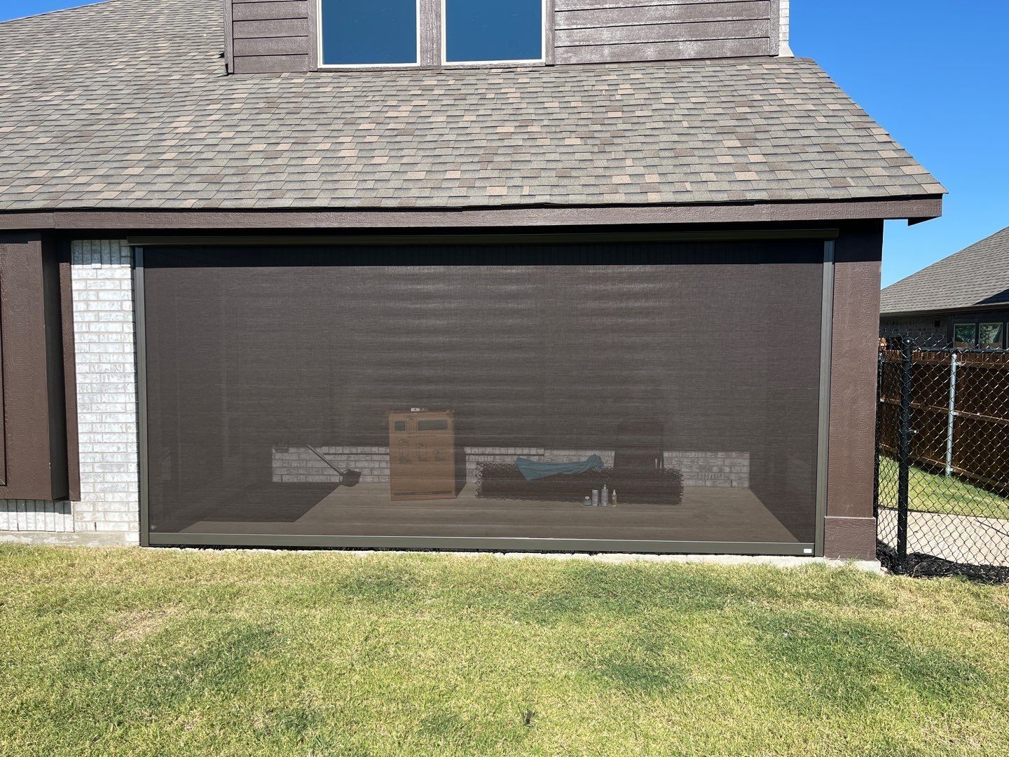 Dark brown outdoor screen attached to a house. Green grass in the foreground.