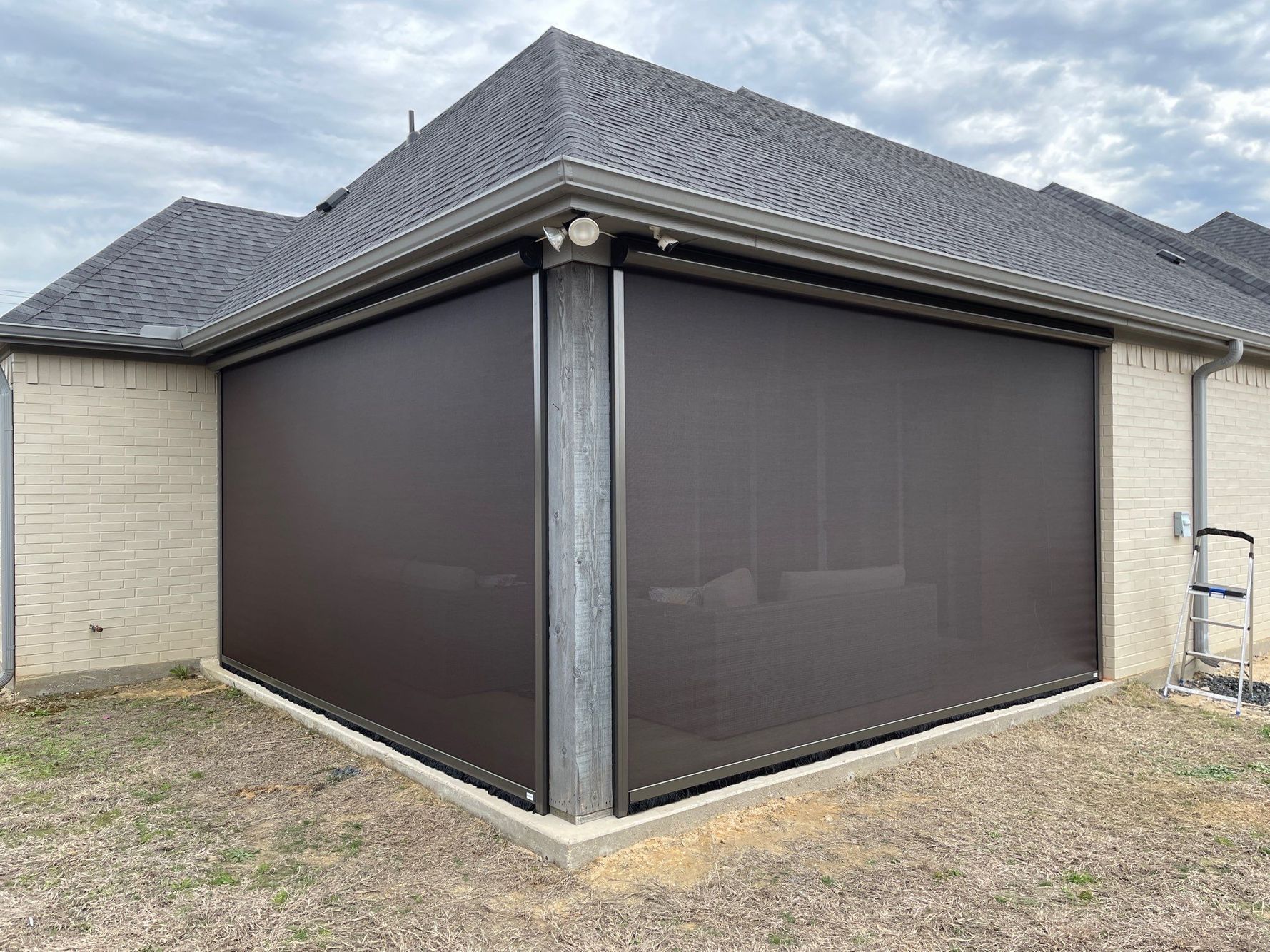 Brown outdoor retractable screens enclose a brick patio under a roof.