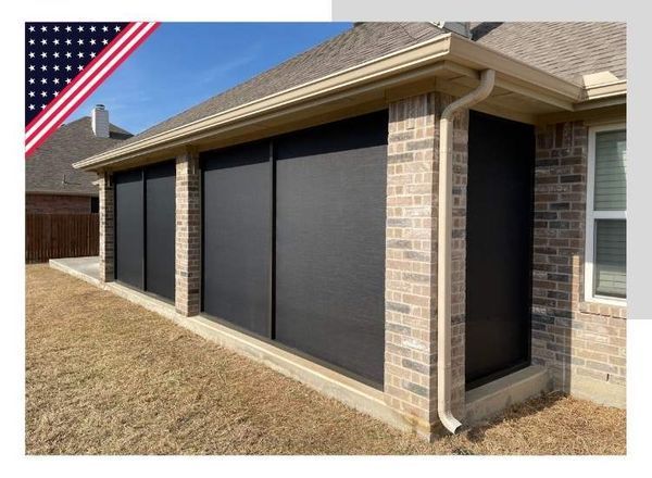 Black outdoor roller shades on a brick patio, against a clear sky.