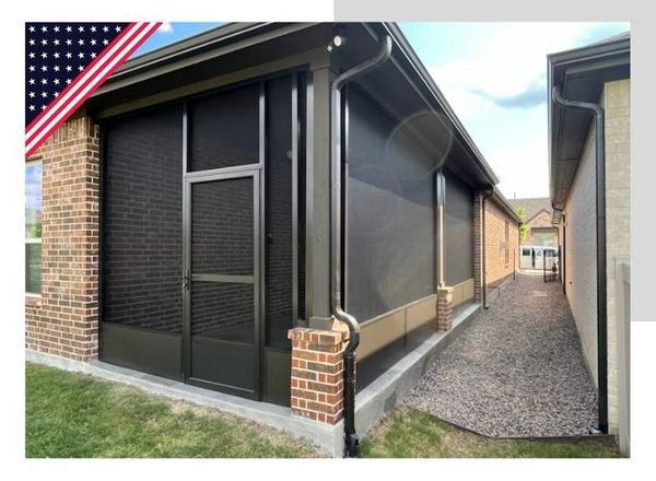 Screened-in porch attached to brick house, brown screens, black trim, gravel path, American flag.