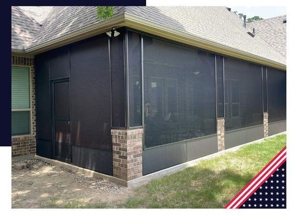 Black screened-in porch with brick accents, attached to a house with a door, on a grassy area.