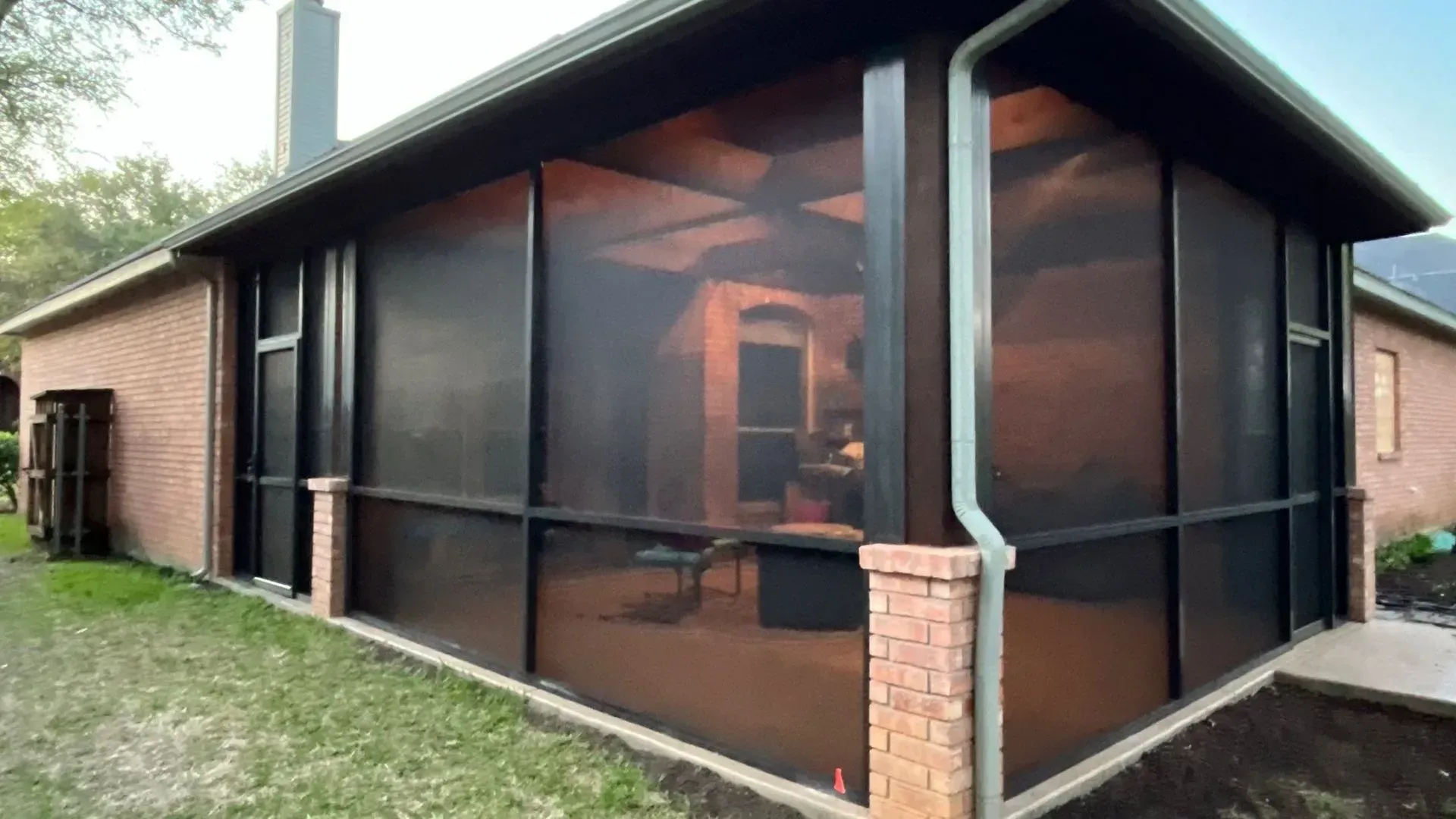 Screened patio enclosure on a brick house with dark mesh walls and a sloped roof