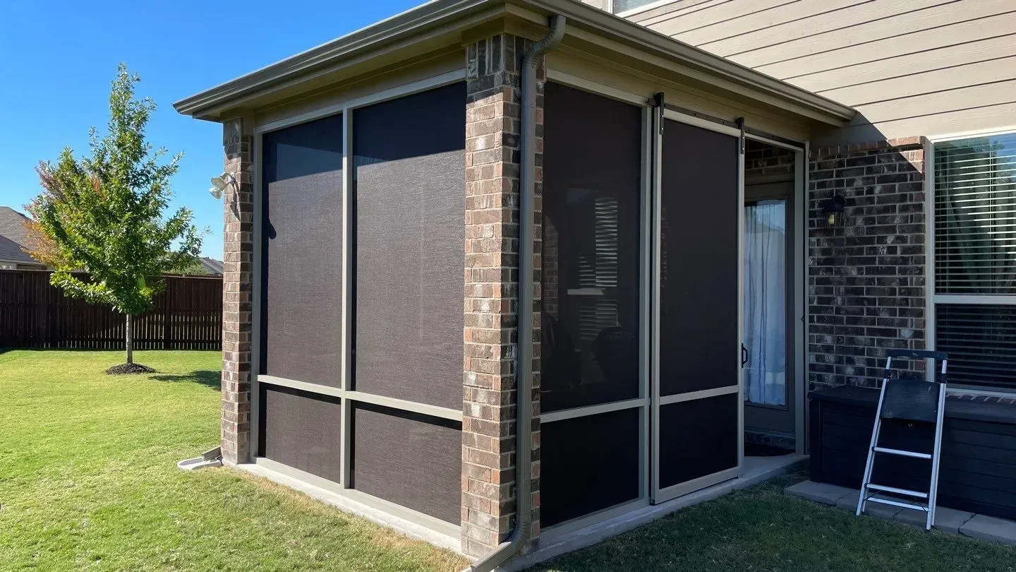 Screened backyard patio attached to a brick house, with lawn and a ladder nearby.