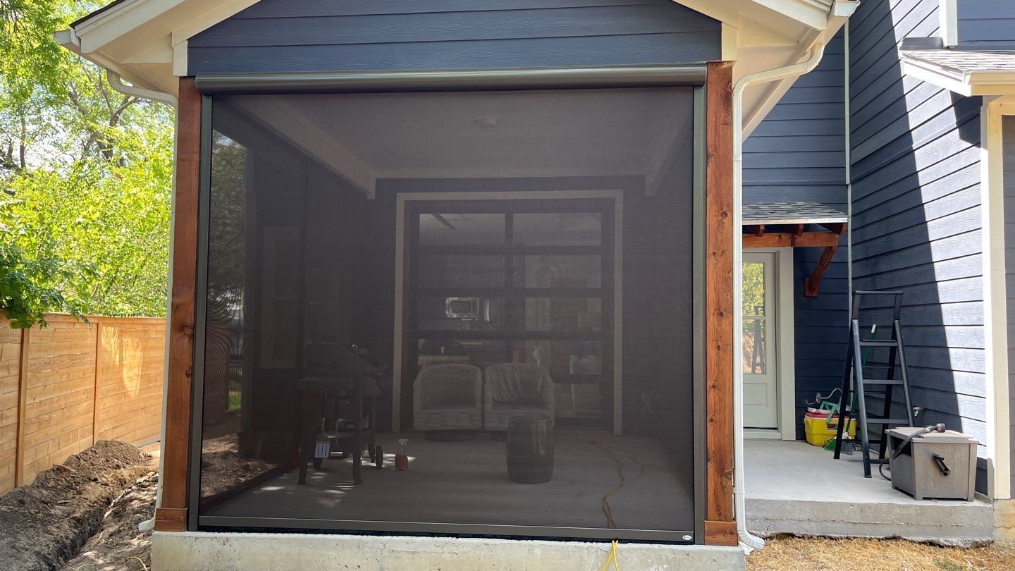 Porch with retractable screen, wooden frame, dark mesh, facing a garage. Blue siding and natural wood trim visible.