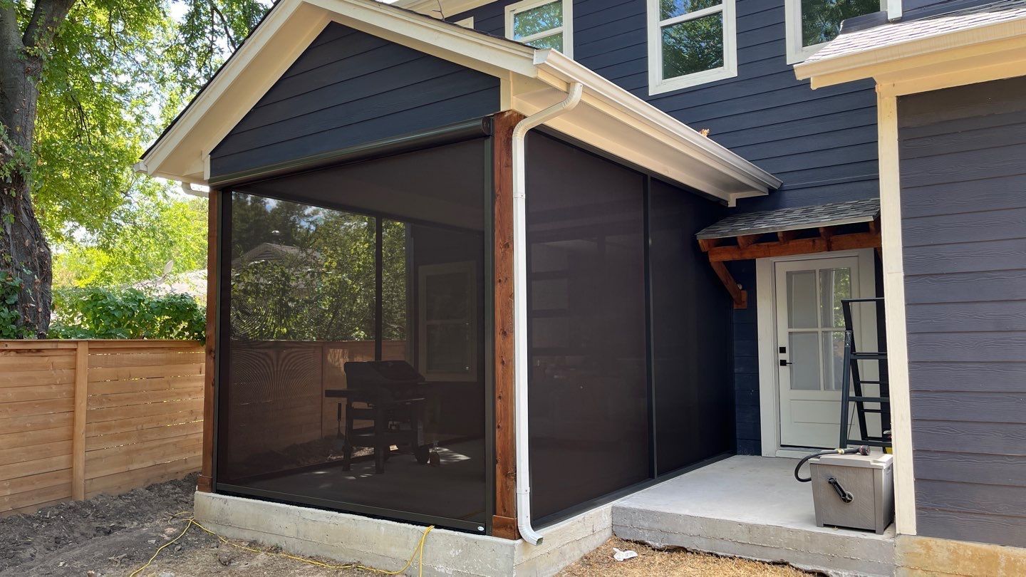 Screened-in porch attached to a blue house, dark brown screen panels. White trim and roof, concrete patio.