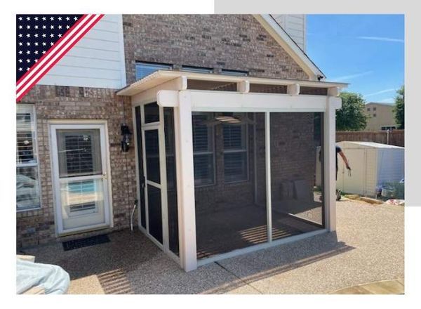 Screened-in patio extension attached to a brick house. White frame, black screens, and concrete flooring.